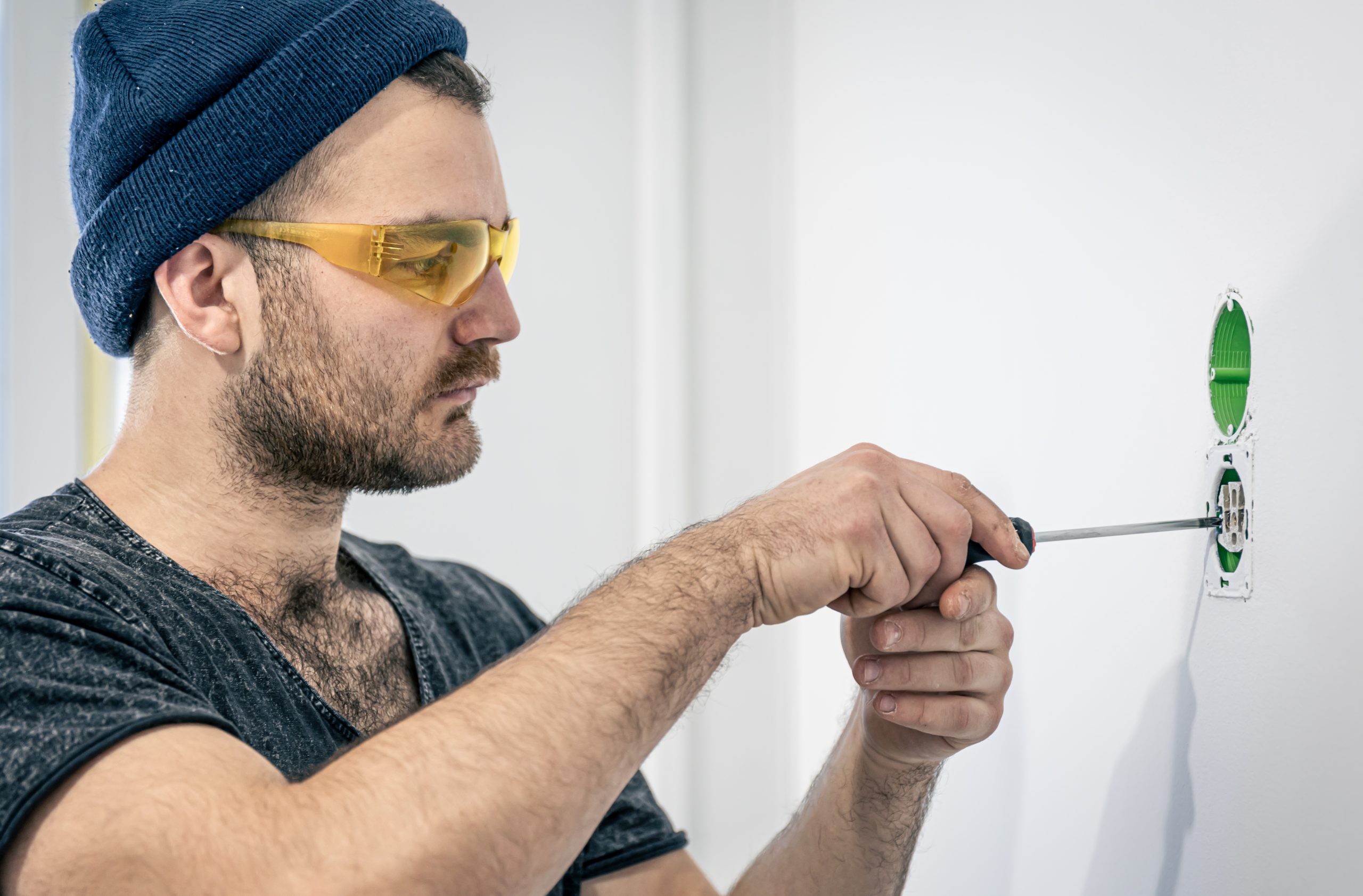 Attractive male electrician repairing an outlet, installing an outlet indoors.